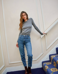 Woman in gray sweater and blue jeans standing on a staircase with decorative railings.