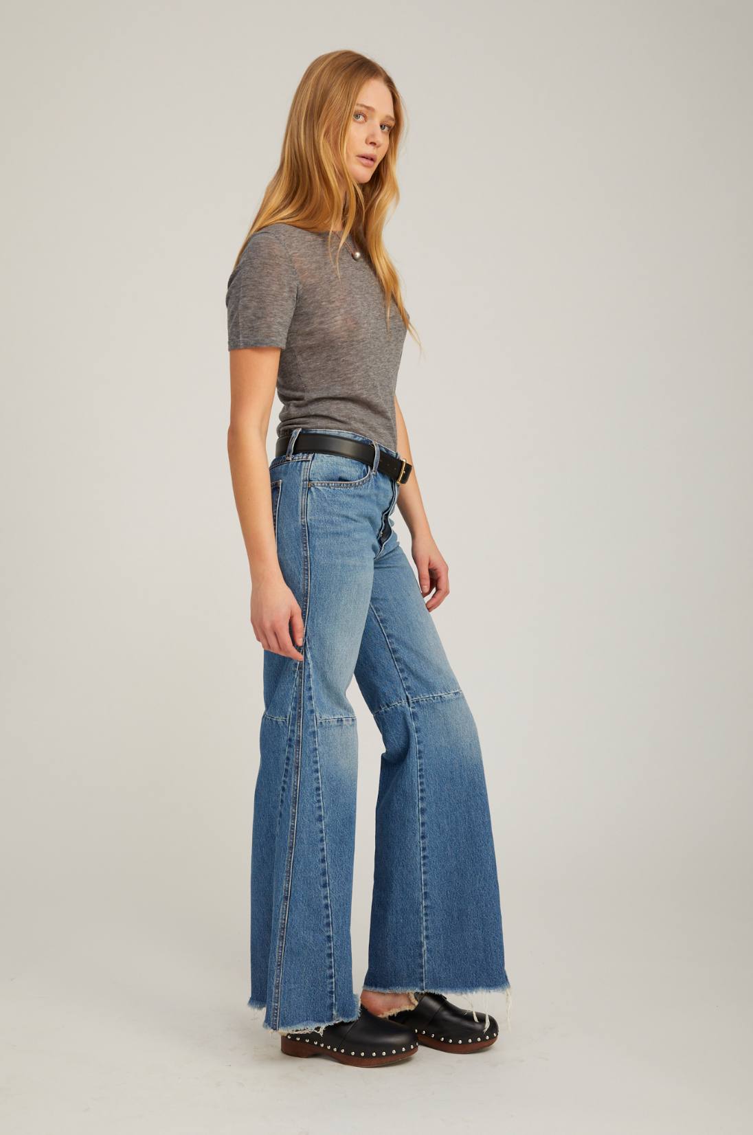 Woman wearing a gray top and blue flared jeans on a plain background