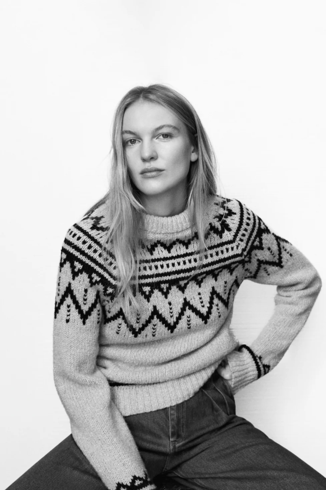 Person wearing a patterned sweater sitting on a white background