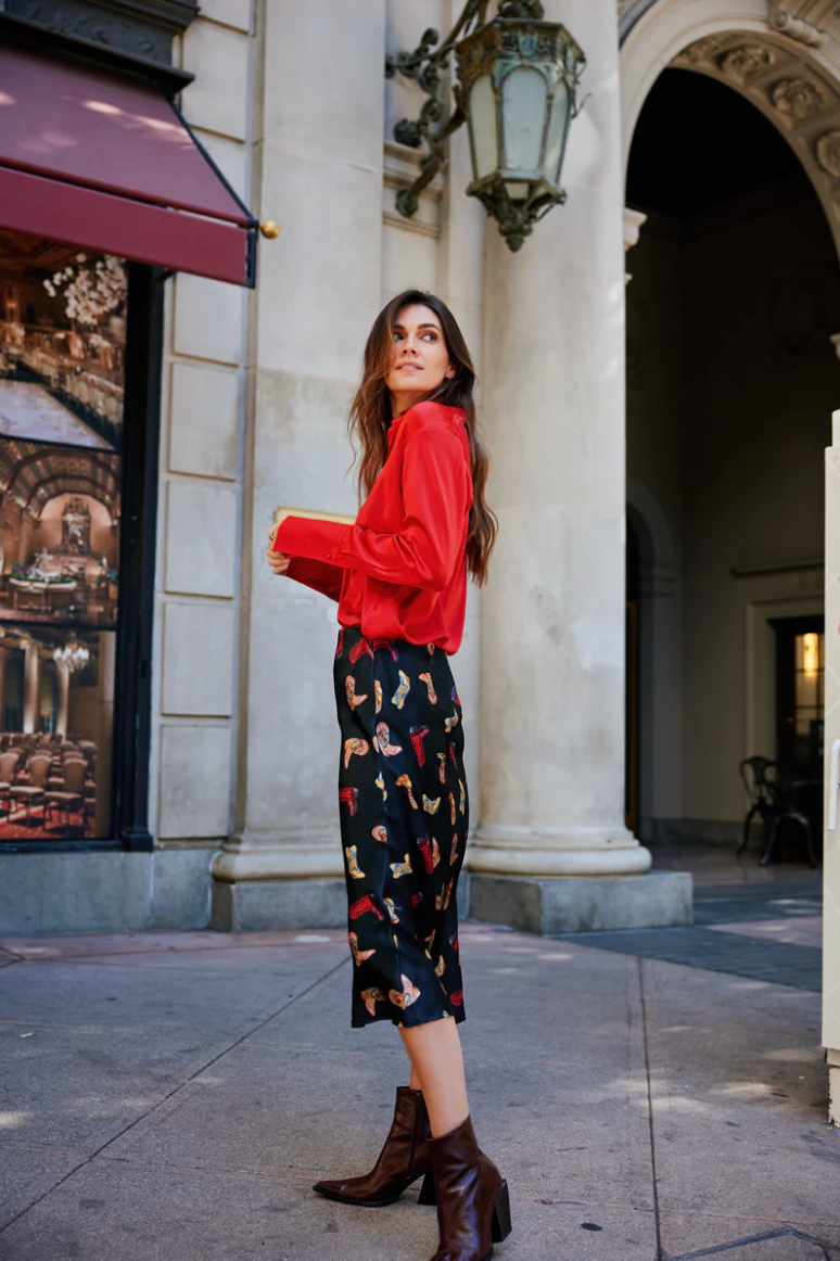 Woman in a red sweater and patterned pants standing in an urban setting.