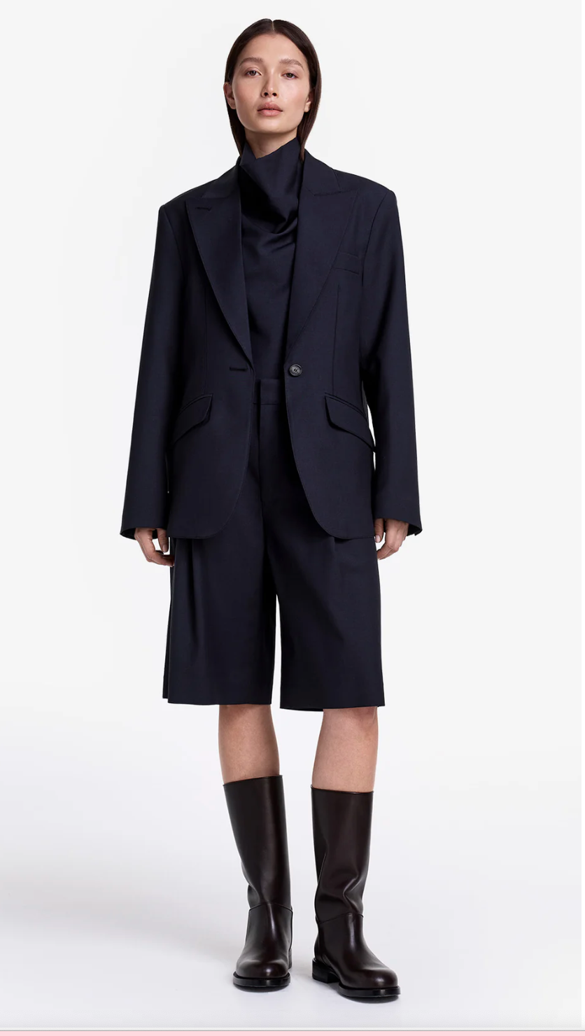 Person wearing a dark navy suit with a high collar and knee-length pants on a white background